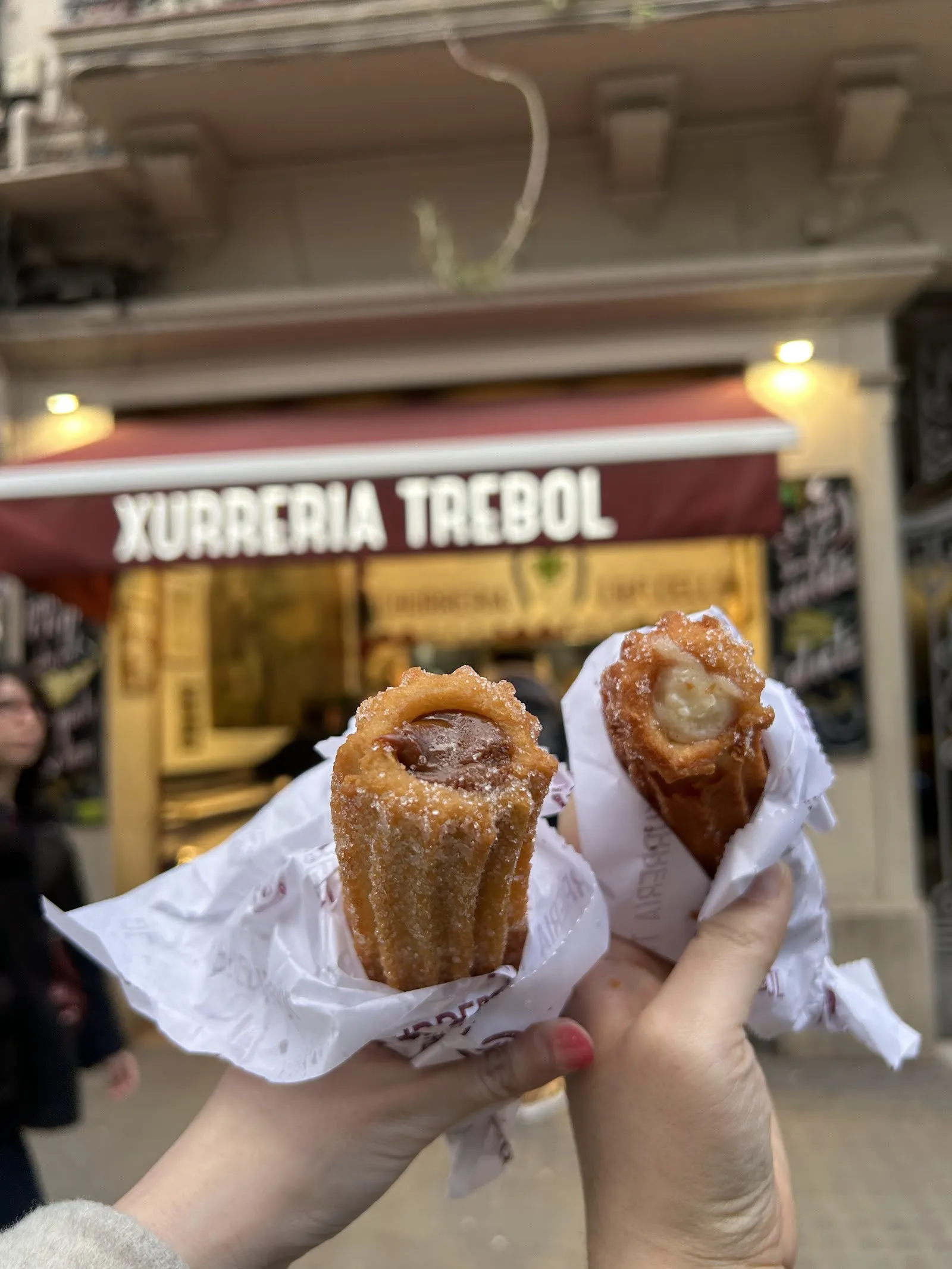 Two filled churros in hand, outside the shop.