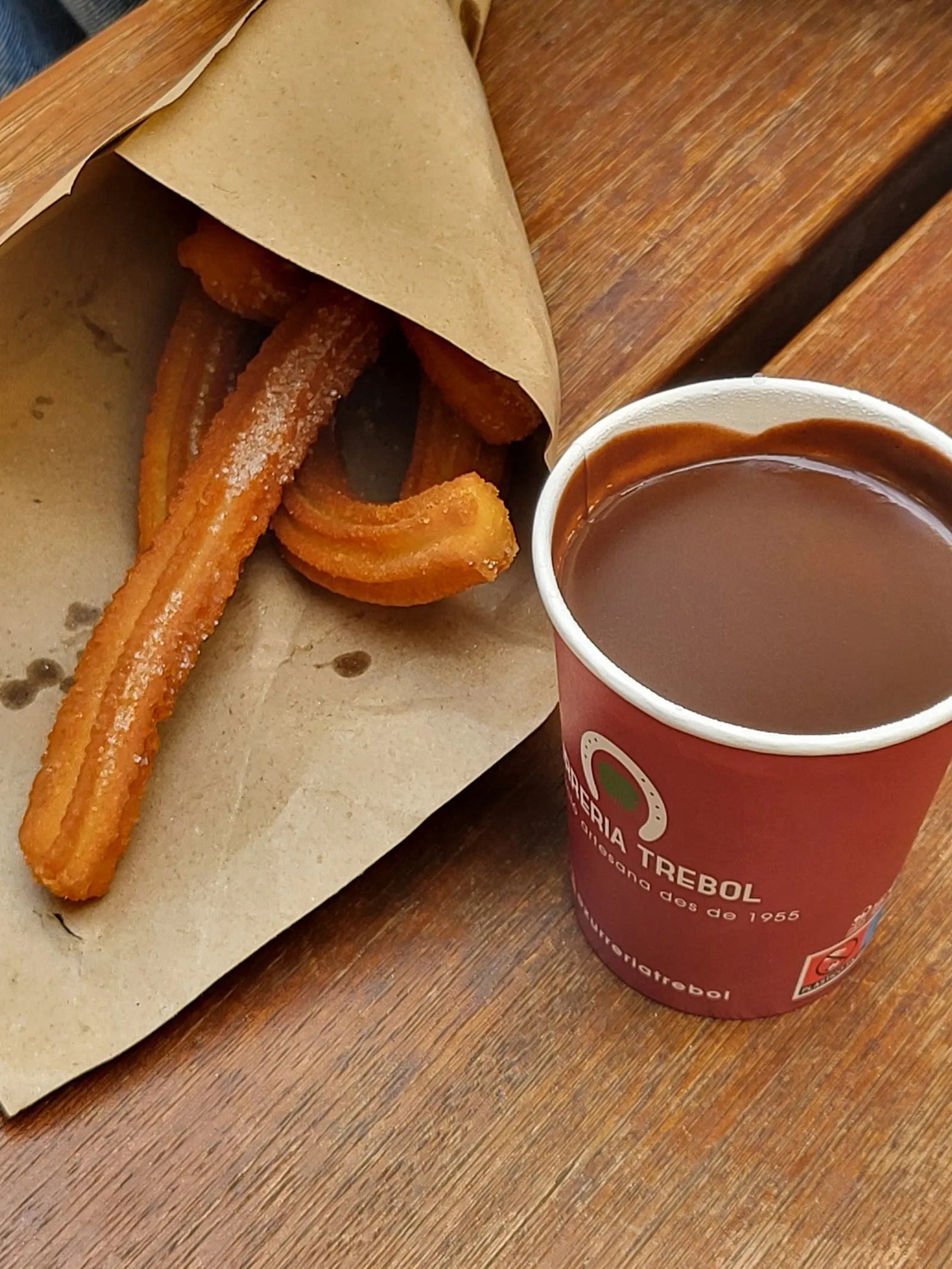 Sugared churros in a paper cone and a cup of Trébol hot chocolate.