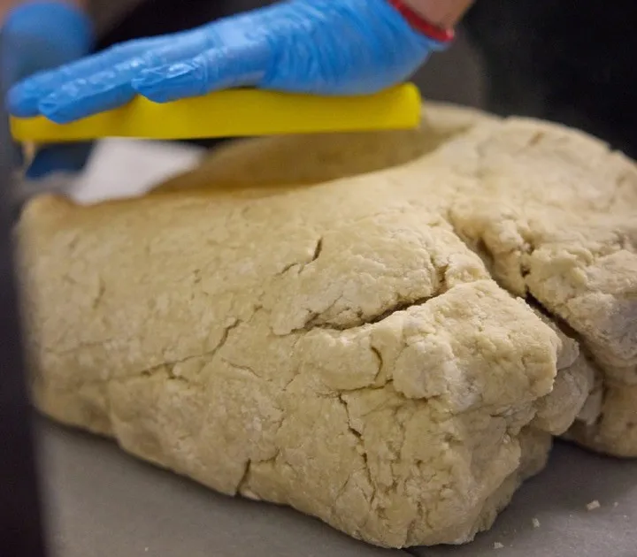 A gloved hand flattening the churro dough on the kitchen worktop.